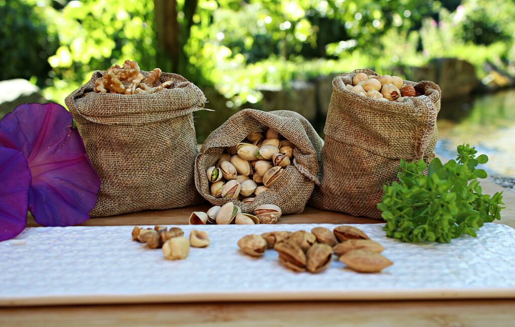 Jute sacks with pistachios walnuts and peanuts placed on wooden table in park near pond on sunny day